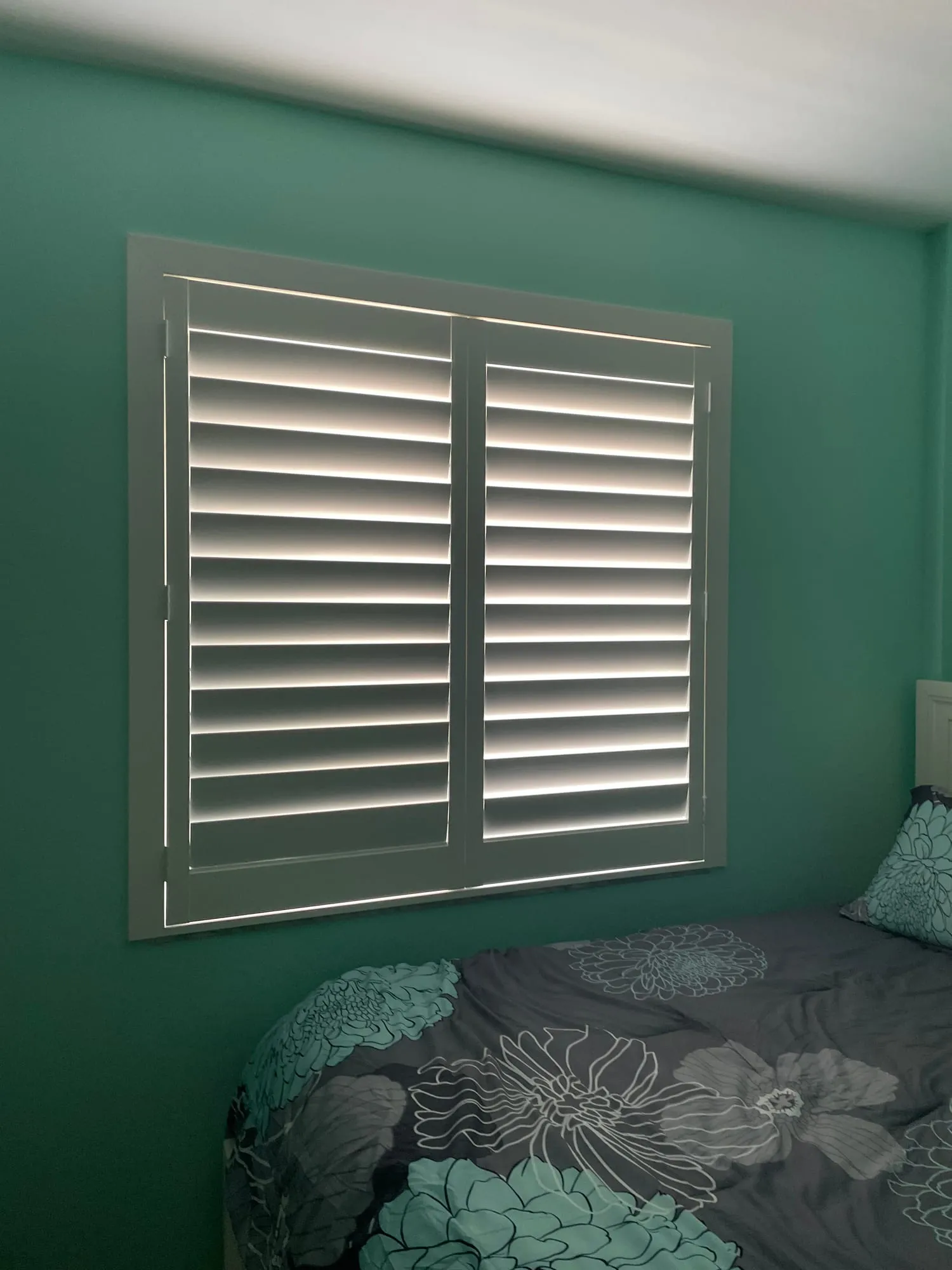 White shutter with a mid-rail on a deep green bedroom wall